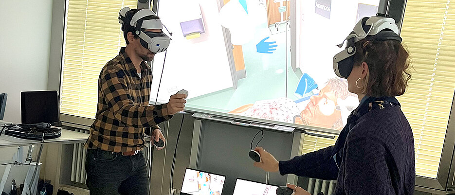 Ein interprofessionelles Team aus Pflegeschüler (links) und Medizinstudentin (rechts) behandelt einen virtuellen Patienten mit Magenblutung. Die Teilnehmenden sehen das Szenario auf ihren VR-Brillen, im Hintergrund wird die Ansicht für das Studienpersonal auf einen Projektor übertragen.