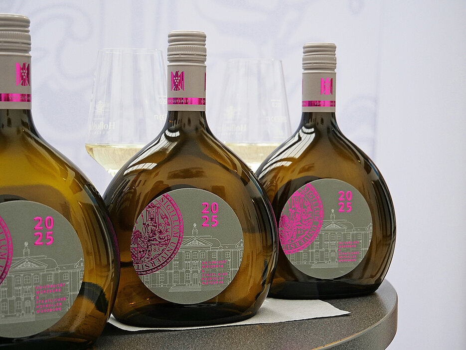 Drei Flaschen des UniWeins stehen in einer Reihe auf einem Tisch.