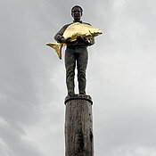 Das Kunstwerk „Der Diez“ in Dießen am Ammersee zeigt einen Mann, der einen goldenen Karpfen hält. Das Denkmal symbolisiert die Bedeutung der Fischerei für die Menschen der Region.